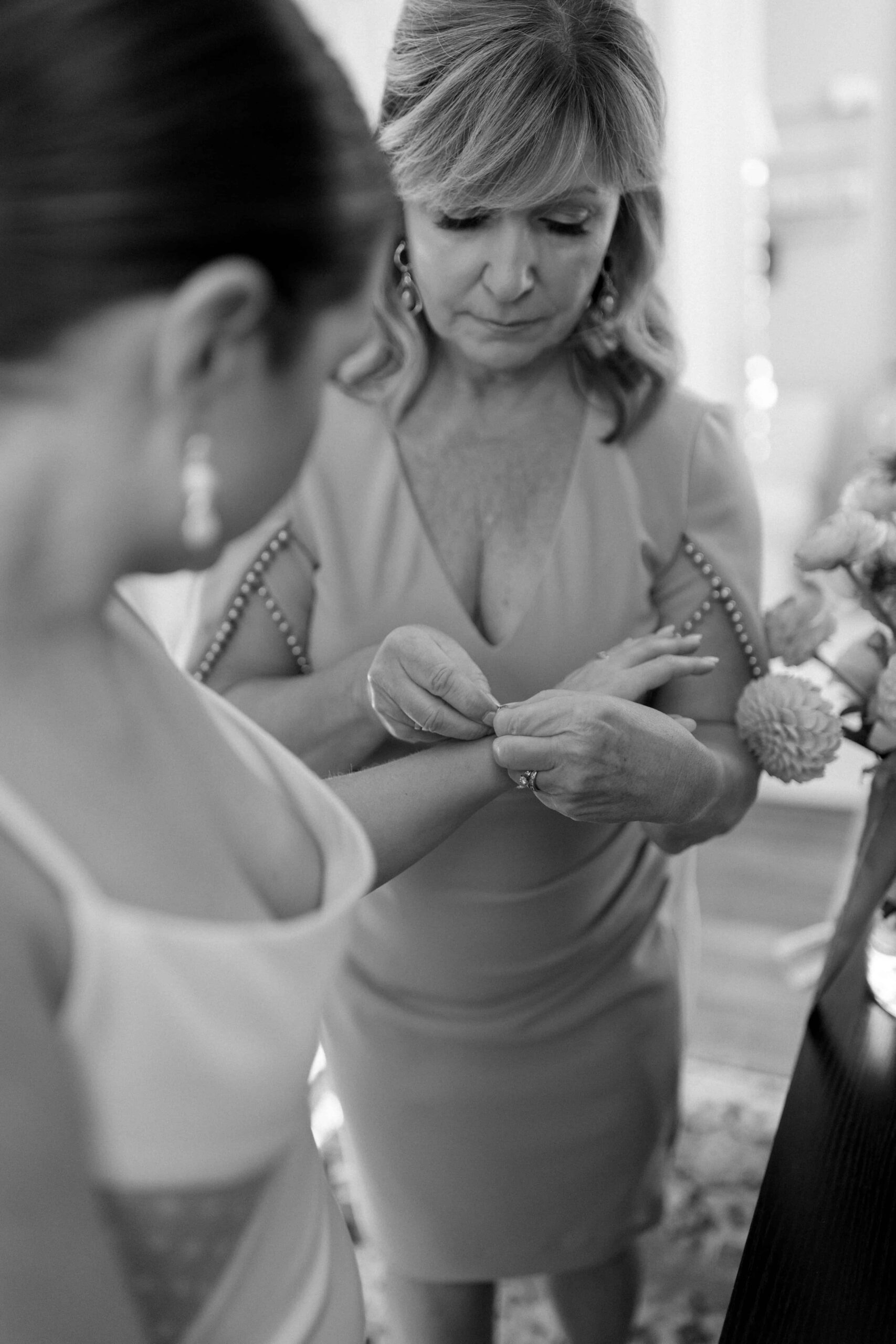 The bride's mom is helping her daughter put on a bracelet. 