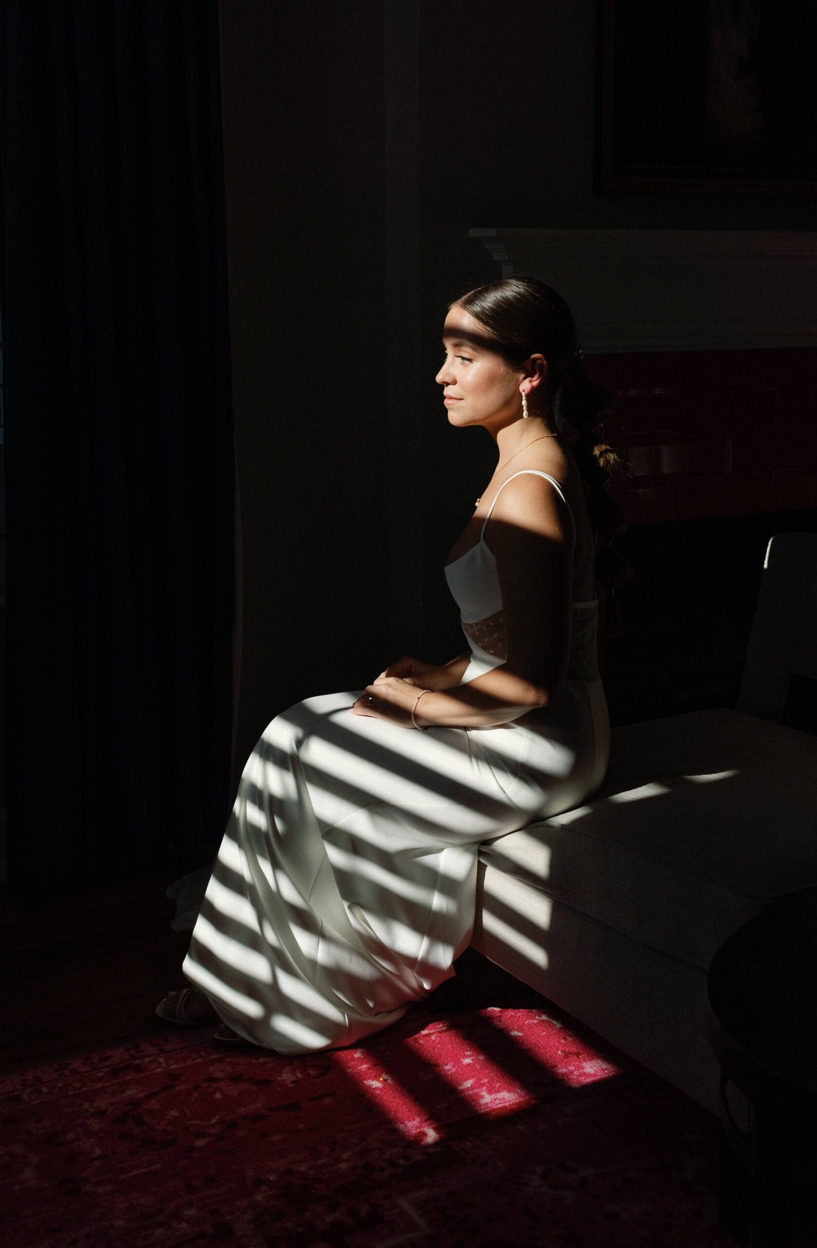 The bride is sitting in the chair with harsh light and shadows on her face.