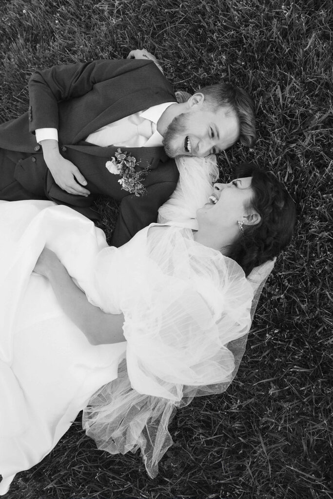 bride and groom laying in the grass smiling